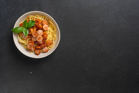 Spaghetti with sliced sausages and basil in white bowl on black background. High quality photoの写真素材