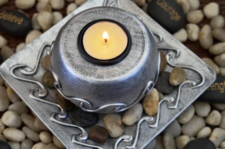 A top view image of a lite tea light candle on a metal candle holder surrounded by pebbles.の写真素材