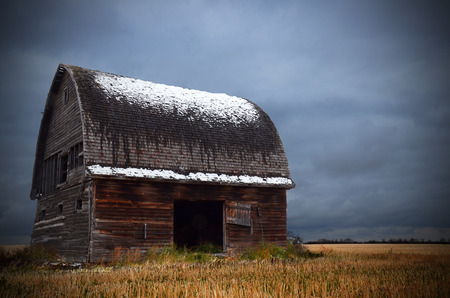 An image of an old run down barn with snow on the roof and storm clouds in the background.の写真素材