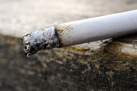 A close up image of a burning cigarette on the edge of a wooden table.の写真素材