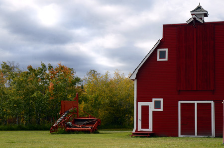 An image of an old combine harvester and a large red barn.のeditorial素材