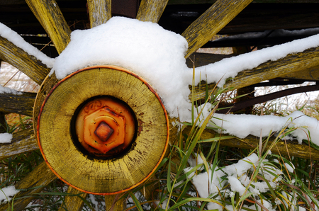 A side view image of a snow covered yellow wooden wagon wheel.の写真素材