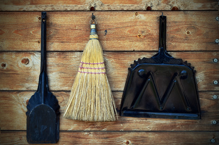 An image of a small corn broom, coal shuttle, and dust pan hanging on a wooden wall.の写真素材
