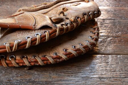A close up image of an old used baseball glove on a wooden table top.の写真素材