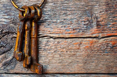 An image of old weathered antique keys handing on a rough wooden wall.の写真素材