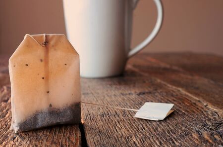 A warm image of a tea bag on a wooden table top with a white tea cup in the background.の写真素材