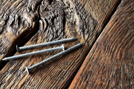 An image of three galvanised nails on a wooden work bench.の写真素材