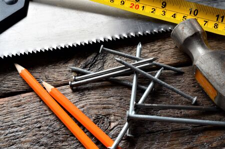 A close up image of an old hammer, saw blade, tape measure, and pencil.