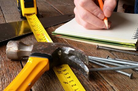 A close up image of an old yellow hammer and tape measure on a wooden workbench.の写真素材