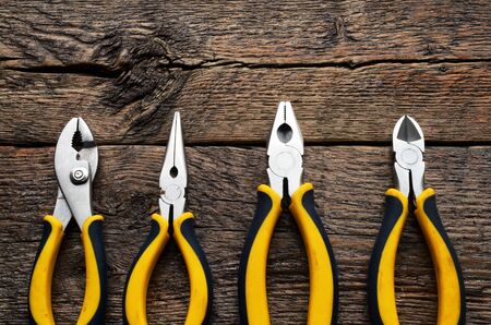 A top view image of four pairs of pliers on a wooden workbench.