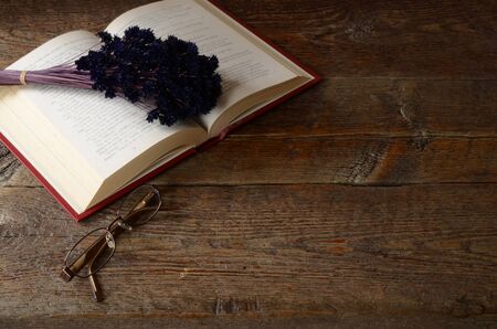 A top view image of a single open book and pair of old eye glasses on a old wooden table top.の写真素材