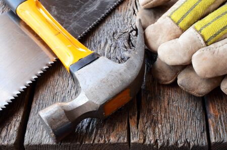 A close up image of an old hammer and work gloves on a wooden workbench.の写真素材