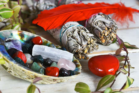 An image of several tumbled healing crystals in an abalone shell with white sage bundles and sacred feather.の写真素材