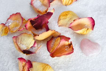 A top view image of white bath salts with dried yellow and red rose petals.の写真素材