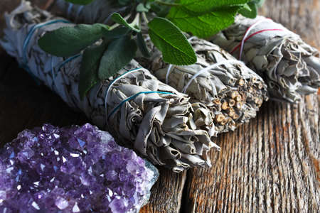 A close up image of an brilliant amethyst geode and white sage on a dark wooden table.の写真素材