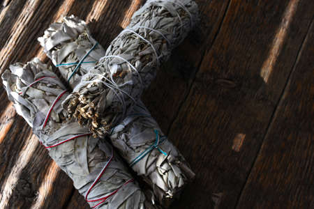 A close up image of three white sage smudge bundles on an old wooden table.の写真素材