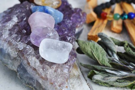A close up image of chakra crystals charging on an amethyst geode with sage and palo santo smudge sticks.の写真素材