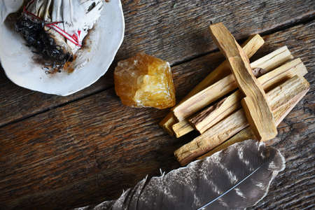A top view image of palo santo smudge sticks with honey calcite crystal and sacred feather on a dark...