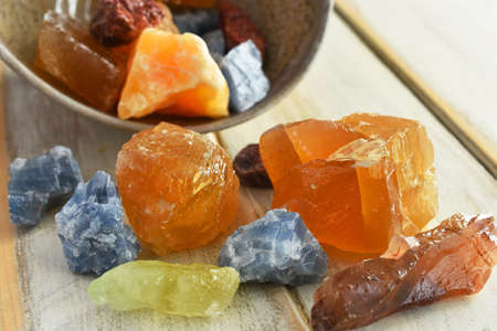 A close up image of a hand made pottery bowl and red, yellow, blue, and green calcite crystals.