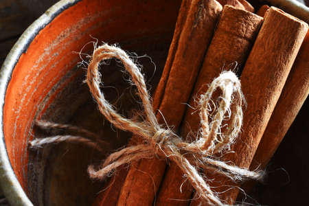 A close up image of several brown cinnamon sticks in a reddish brown handmade pottery bowl.