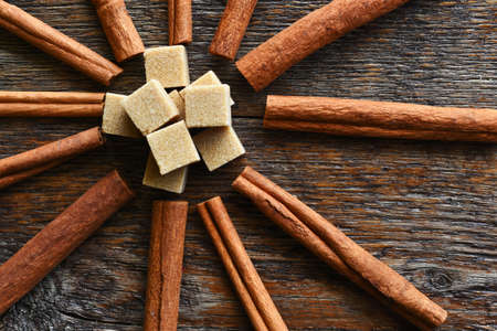 A top view image of several cinnamon sticks and brown sugar cubes on a dark wooden table.