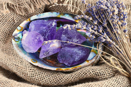 A close up image of several rough pieces of amethyst crystal in an abalone shell with dried lavender flowers.の写真素材