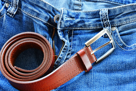 A close up image of an old reddish brown leather belt and a pair of faded blue jeans.の写真素材