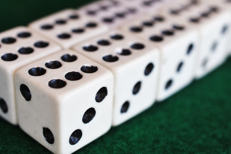 A close up image of several black and white dice lined up in a row on dark green felt cloth.の写真素材