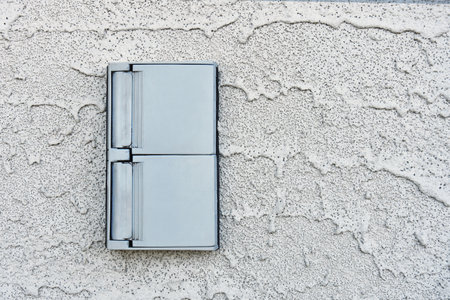 An image of a grey out door electrical socket on a grey stucco wall.の写真素材
