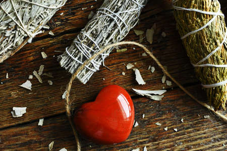 A close up image of a variety of sacred smudge bundles with selenite and red jasper crystals on a dark wooden table top.の写真素材