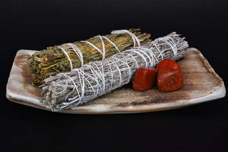 A close up image of two smudge stick bundles and red jasper crystals on a hand made pottery plate.の写真素材