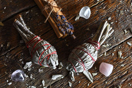 A top view image of two sage smudge sticks and healing crystals on a dark wooden table top.