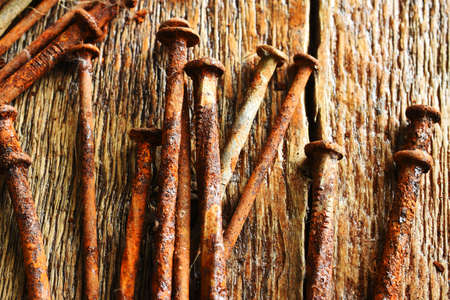 A close up image of several old and very rusted nails on a dark wooden table.の写真素材