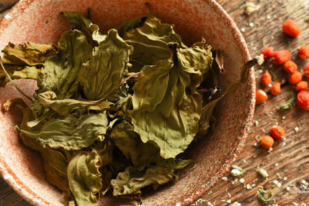A top view image of a rustic pottery bowl filled with dried plantain leaves with dried rose hips on...