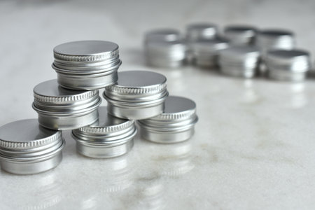 A close up image of several small silver metal sample tins on a white marble table top.の写真素材