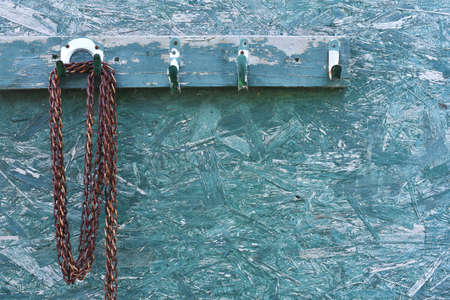 An image of an old rusted chain hanging on a green plywood wall.の写真素材
