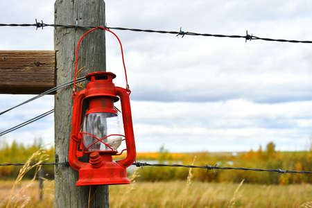 An image of an old vintage lantern hanging on a wooden fence post.の写真素材