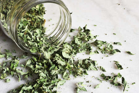 A close up image of home grown organic oregano spilling out of a glass jar on to a marble table top.の写真素材