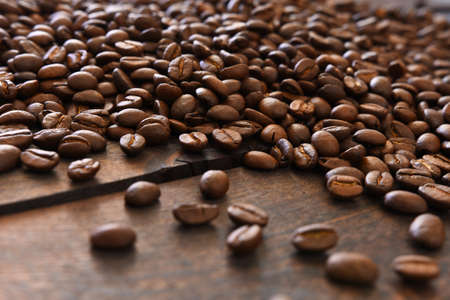 A close up image of dark roasted coffee beans spilled on a dark wooden table top.