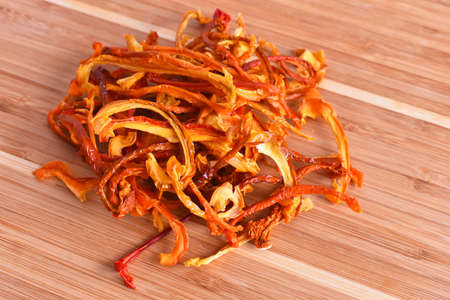A top view image of dehydrated yellow and red organic peppers on a wooden cutting board.