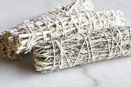 A close up image of three white sage smudge sticks on a white marble table top.の写真素材