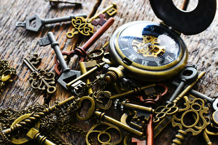 A close up image of several old vintage keys with pocket watch on a dark wooden table top.