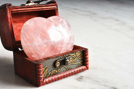 A close up image of a heart shaped rose quartz crystal in a small wooden box.の写真素材