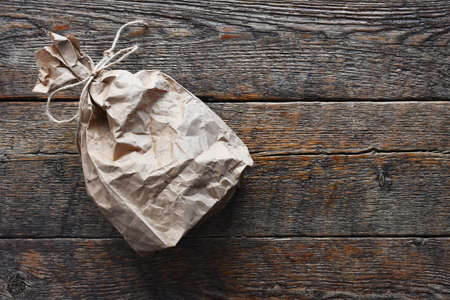 An image of a wrinkled brown paper bag tied with string on an old wooden table top.の写真素材