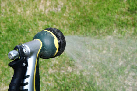 A close up image of a dirty garden hose nozzle spraying a stream of water onto green grass.の写真素材