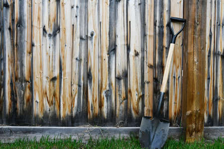 An image of an old metal garden shovel leaning on a weathered wooden fence.の写真素材