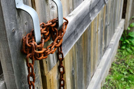A close up image of a very rusted chain wrapped around handles on a weathered old wooden gate.の写真素材