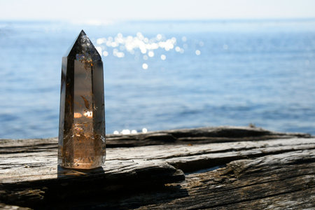 Tall smoky quartz crystal tower resting on a piece of driftwood with the Pacific Ocean in the...