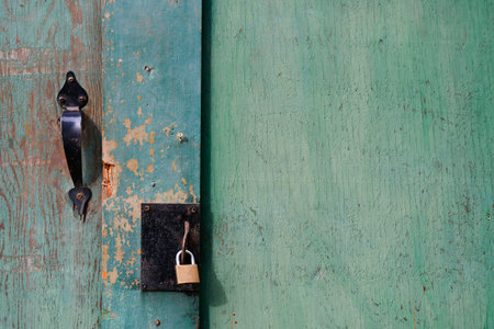 An old wooden doorway with faded and weathered paint and locked with a shiny brass padlock.