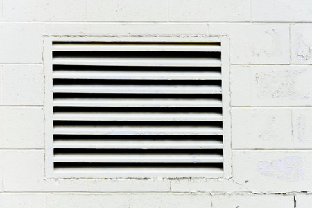 An abstract image of a large square air intake vent on a white exterior brick wall.の写真素材